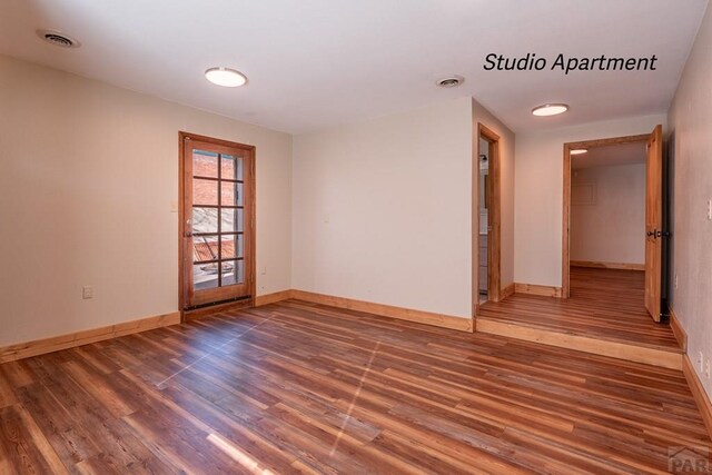 unfurnished room featuring dark wood-style flooring, visible vents, and baseboards