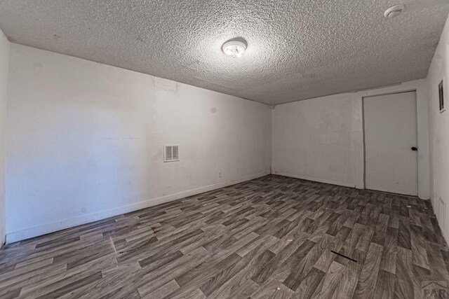 spare room with dark wood-style flooring, visible vents, a textured ceiling, and baseboards