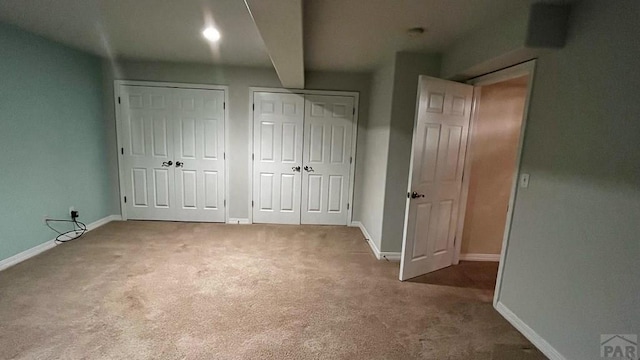 unfurnished bedroom with carpet flooring, two closets, and baseboards