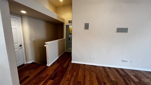 hallway with dark wood-style flooring, visible vents, an upstairs landing, baseboards, and washer / dryer