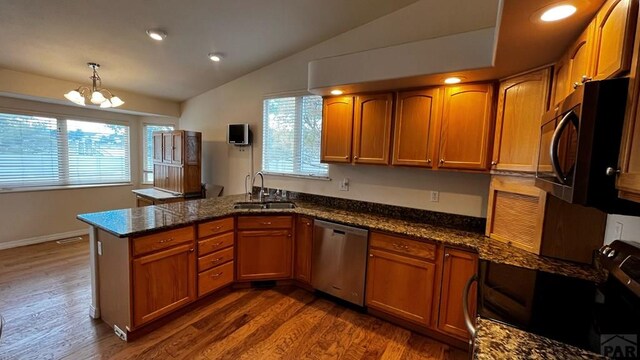 kitchen with brown cabinetry, a peninsula, hanging light fixtures, stainless steel dishwasher, and a sink