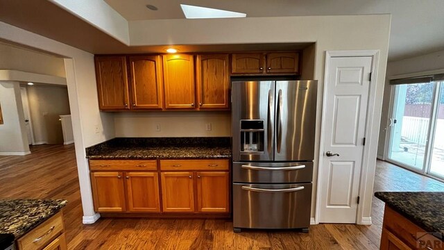 kitchen with brown cabinets, stainless steel fridge, and dark stone counters