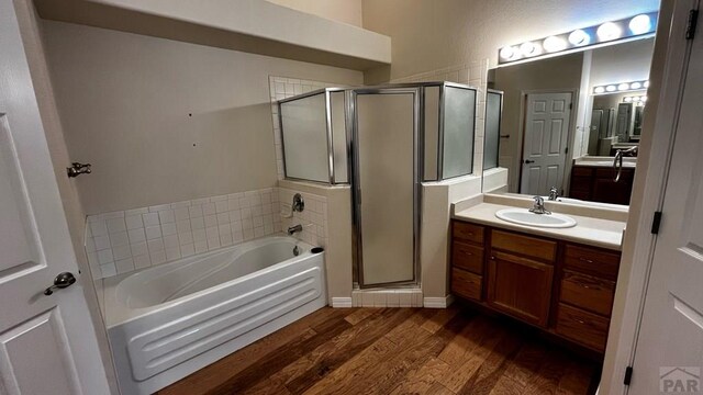 bathroom with a stall shower, vanity, a bath, and wood finished floors