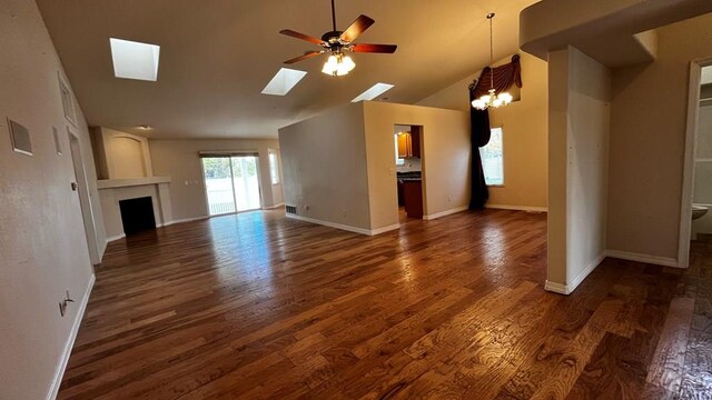 unfurnished living room featuring ceiling fan with notable chandelier, a fireplace, a skylight, baseboards, and dark wood-style floors