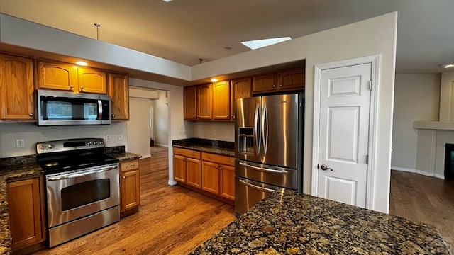 kitchen with brown cabinetry, stainless steel appliances, and dark stone countertops