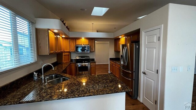 kitchen featuring a peninsula, a skylight, a sink, appliances with stainless steel finishes, and brown cabinets