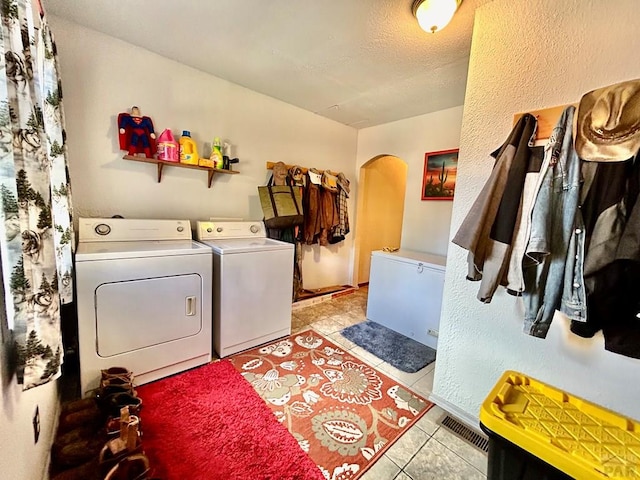 clothes washing area featuring arched walkways, light tile patterned floors, visible vents, washer and dryer, and laundry area