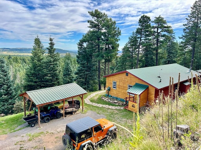 view of side of home with a carport, dirt driveway, metal roof, and a view of trees