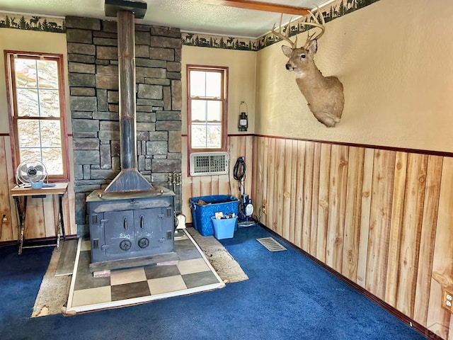 interior space featuring a wainscoted wall, a wood stove, a textured ceiling, wood walls, and dark carpet