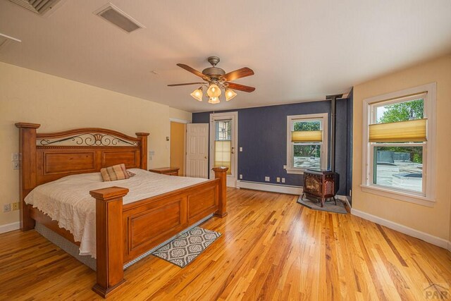 bedroom with a wood stove, light wood-style floors, visible vents, and a baseboard heating unit