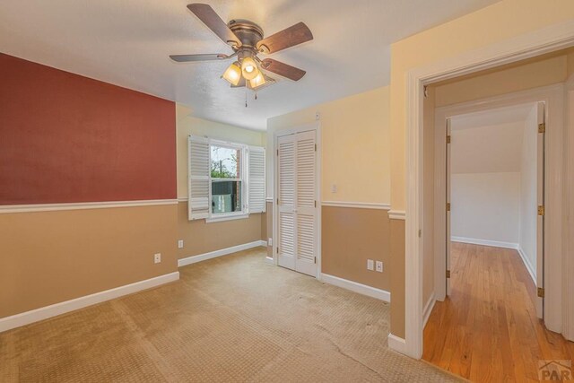 unfurnished bedroom featuring light carpet, ceiling fan, baseboards, and a closet