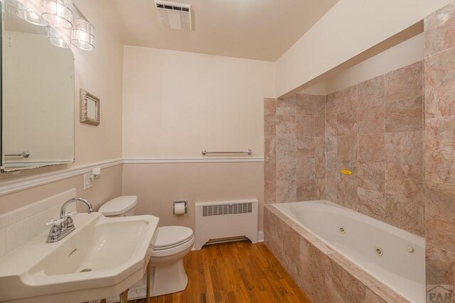 bathroom featuring wood finished floors, a sink, visible vents, radiator, and a whirlpool tub