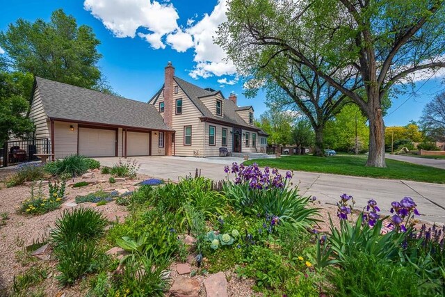 exterior space with a garage, a shingled roof, driveway, a front lawn, and a chimney