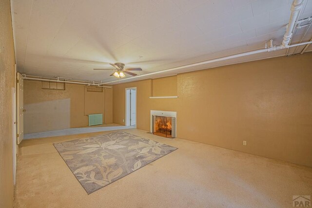 unfurnished living room featuring ceiling fan, radiator heating unit, light colored carpet, and a lit fireplace