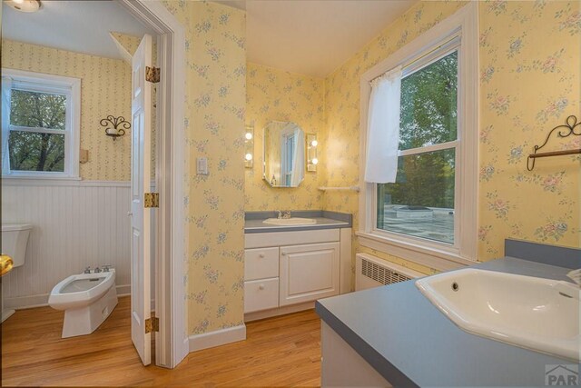 bathroom featuring wallpapered walls, wainscoting, radiator, wood finished floors, and a bidet