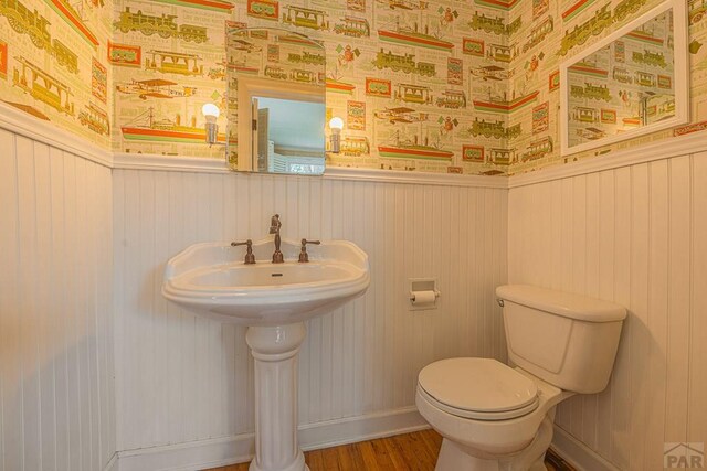 bathroom with a wainscoted wall, wood finished floors, toilet, and wallpapered walls