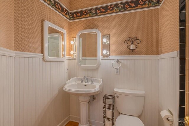 bathroom featuring wainscoting, toilet, and wallpapered walls