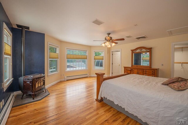 bedroom with light wood-type flooring, a wood stove, visible vents, and baseboard heating