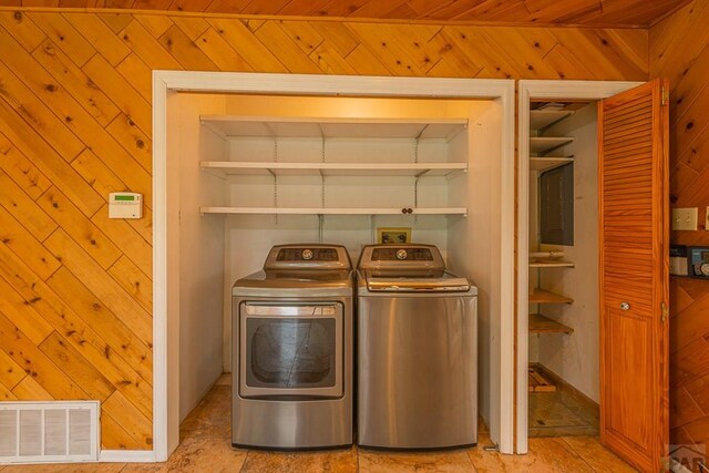 laundry room with laundry area, separate washer and dryer, wood walls, and visible vents