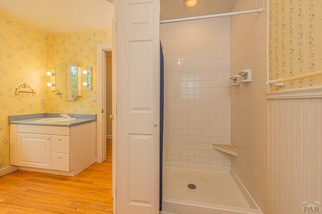 full bathroom with wood finished floors, a shower stall, vanity, and wallpapered walls