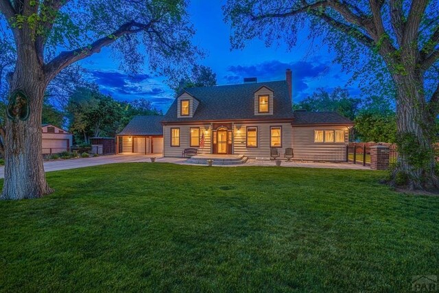 back of house at dusk with a yard, driveway, a chimney, and fence