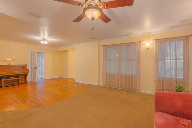 living room featuring baseboards, visible vents, a ceiling fan, ornamental molding, and carpet