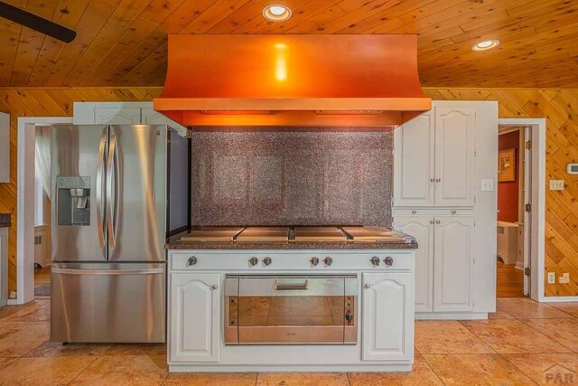 kitchen with wooden walls, wooden ceiling, stainless steel appliances, premium range hood, and white cabinetry