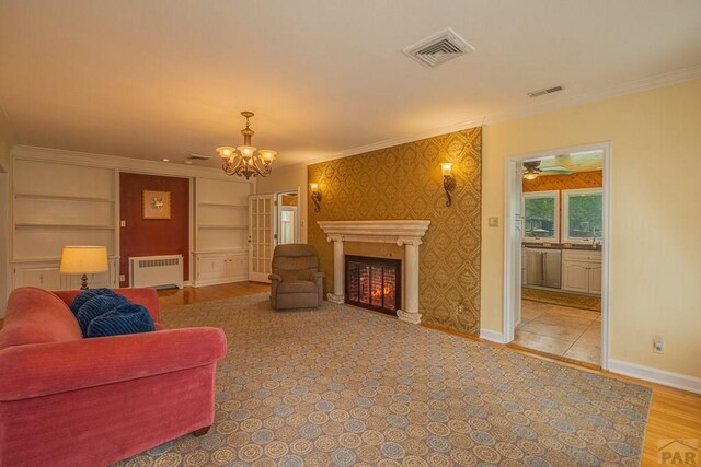 living area with crown molding, visible vents, radiator heating unit, a glass covered fireplace, and baseboards