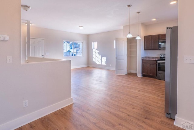 interior space with baseboards, open floor plan, light wood-style floors, appliances with stainless steel finishes, and pendant lighting