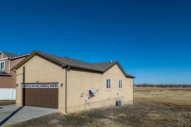 view of side of home with central AC unit, a garage, fence, driveway, and stucco siding