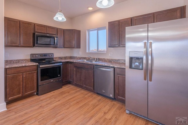 kitchen with light wood finished floors, appliances with stainless steel finishes, dark brown cabinets, pendant lighting, and a sink