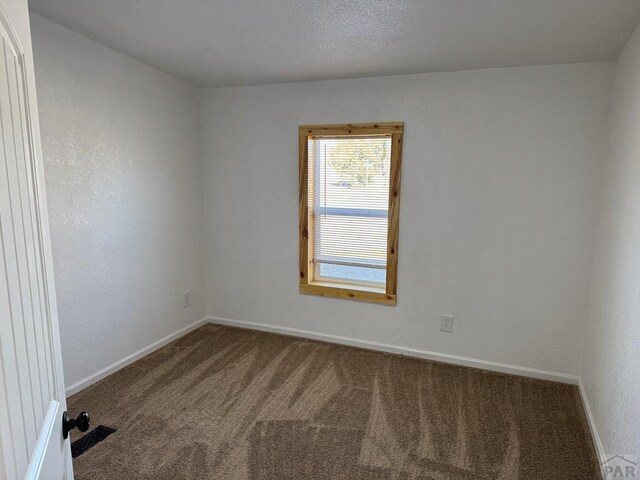 spare room featuring carpet, visible vents, and baseboards