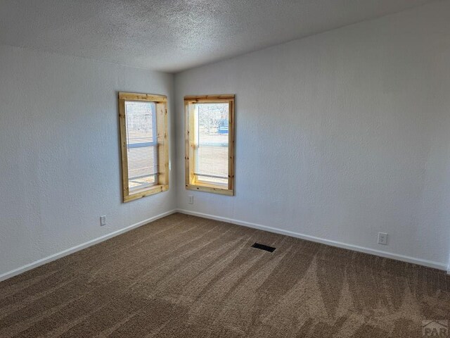 unfurnished room with visible vents, a textured wall, dark carpet, a textured ceiling, and baseboards