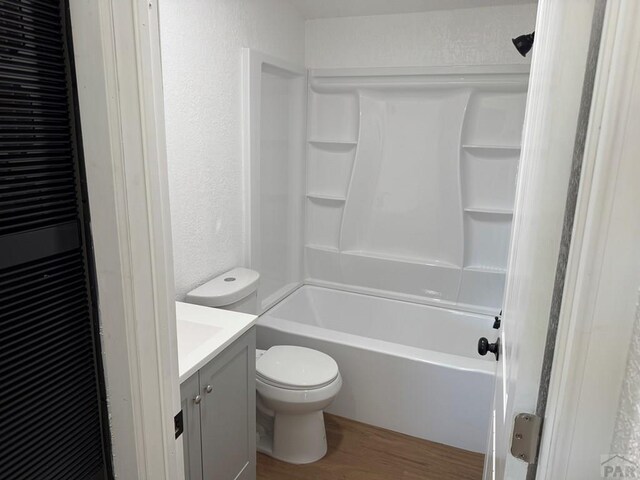 full bathroom with shower / bathing tub combination, a textured wall, toilet, vanity, and wood finished floors