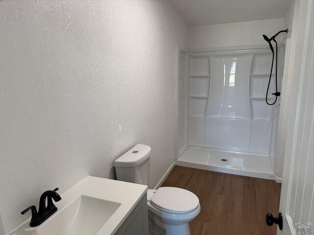 full bath featuring a textured wall, toilet, wood finished floors, vanity, and a stall shower