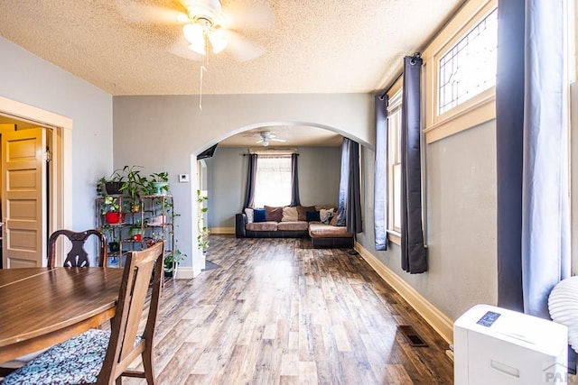 dining space featuring arched walkways, ceiling fan, a textured ceiling, and wood finished floors