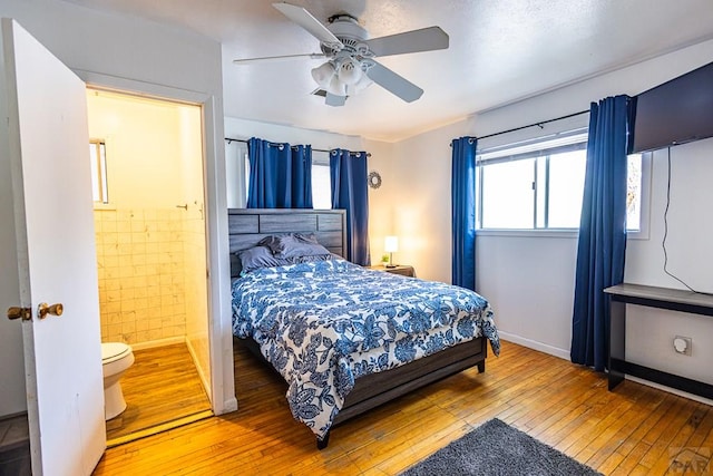 bedroom featuring tile walls, ensuite bath, a ceiling fan, and wood finished floors