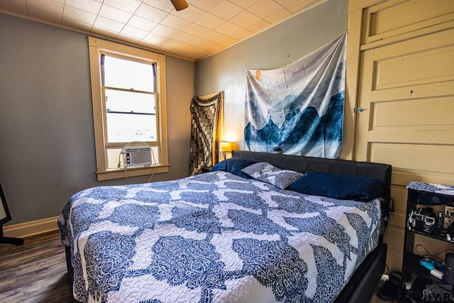 bedroom with a ceiling fan, baseboards, dark wood-type flooring, and cooling unit