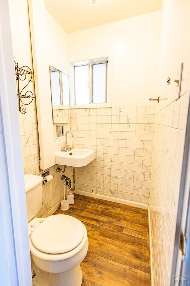 bathroom with baseboards, toilet, wood finished floors, a sink, and tile walls