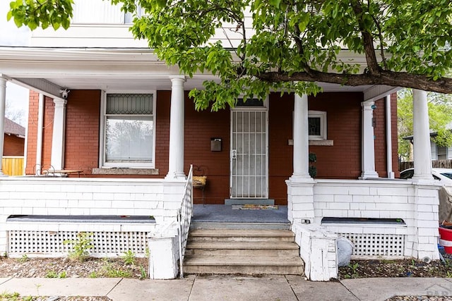 doorway to property with a porch and brick siding