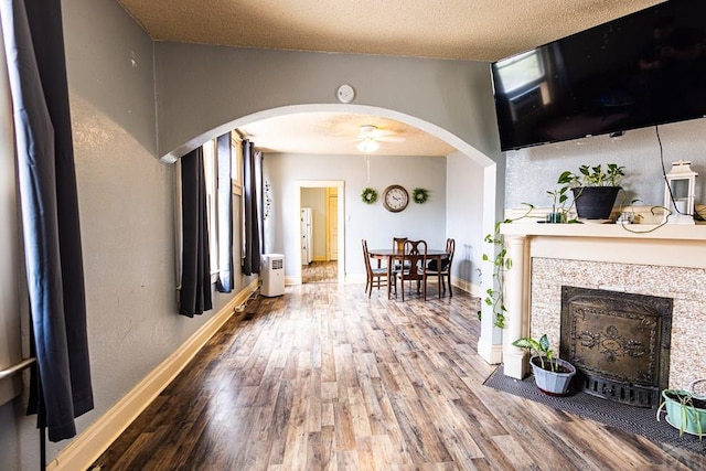 living room featuring baseboards, arched walkways, a fireplace with flush hearth, wood finished floors, and a textured ceiling