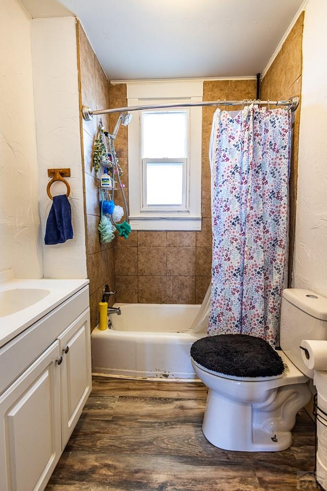 full bathroom with a textured wall, toilet, shower / tub combo with curtain, wood finished floors, and vanity