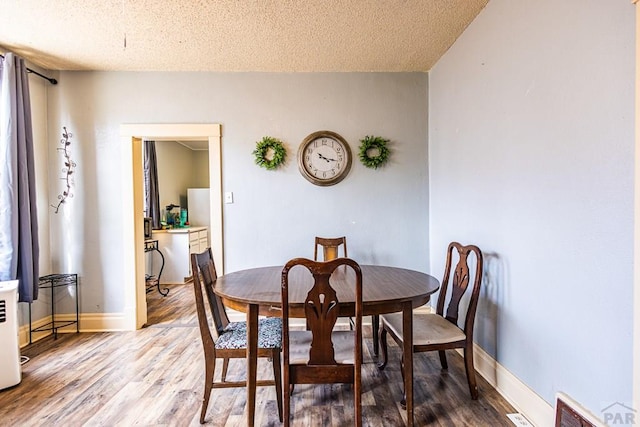 dining area featuring a textured ceiling, baseboards, and wood finished floors