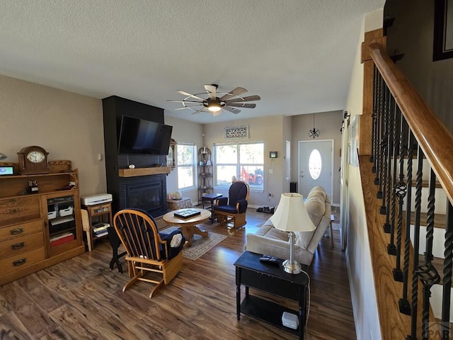 living area featuring a textured ceiling, dark wood finished floors, stairway, a fireplace, and ceiling fan