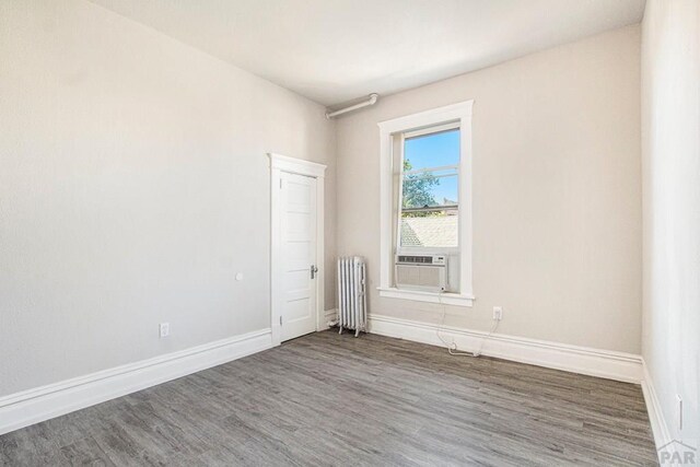 empty room with radiator heating unit, wood finished floors, and baseboards