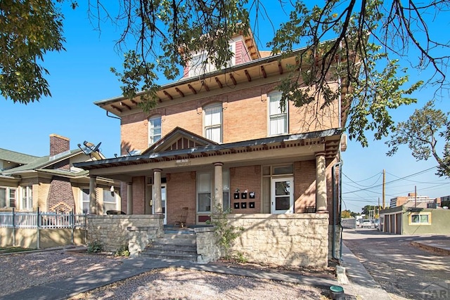 view of front of house with covered porch, brick siding, and fence