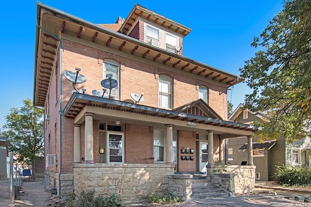 italianate house with stone siding, a porch, and brick siding