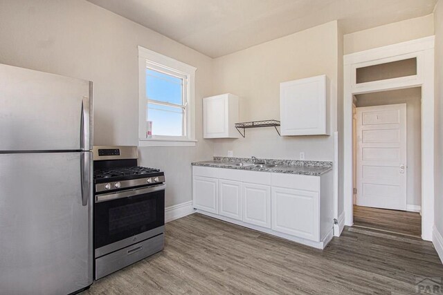 kitchen with stainless steel appliances, white cabinetry, a sink, wood finished floors, and baseboards