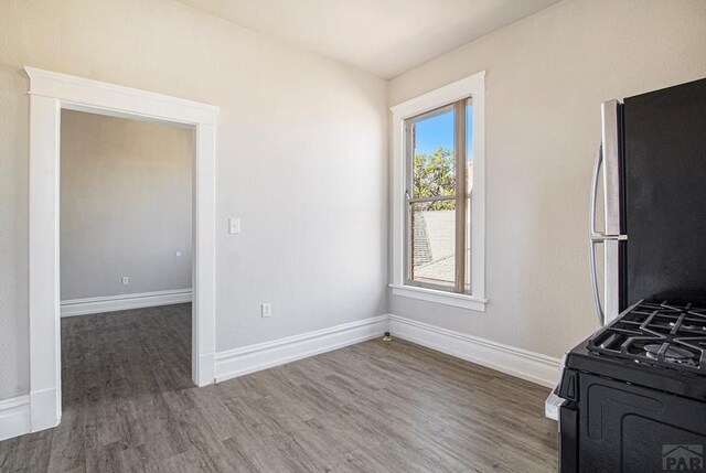 kitchen featuring black gas range, baseboards, dark wood-type flooring, and freestanding refrigerator