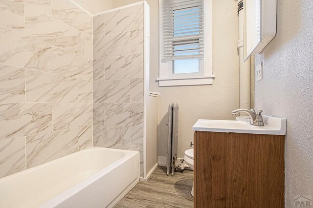 bathroom with a textured wall, toilet, bathing tub / shower combination, wood finished floors, and vanity